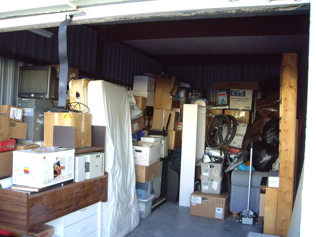 Large, open unit at a storage facility giving a preview of the contents before an auction. Unit is filled with various household items and boxes.